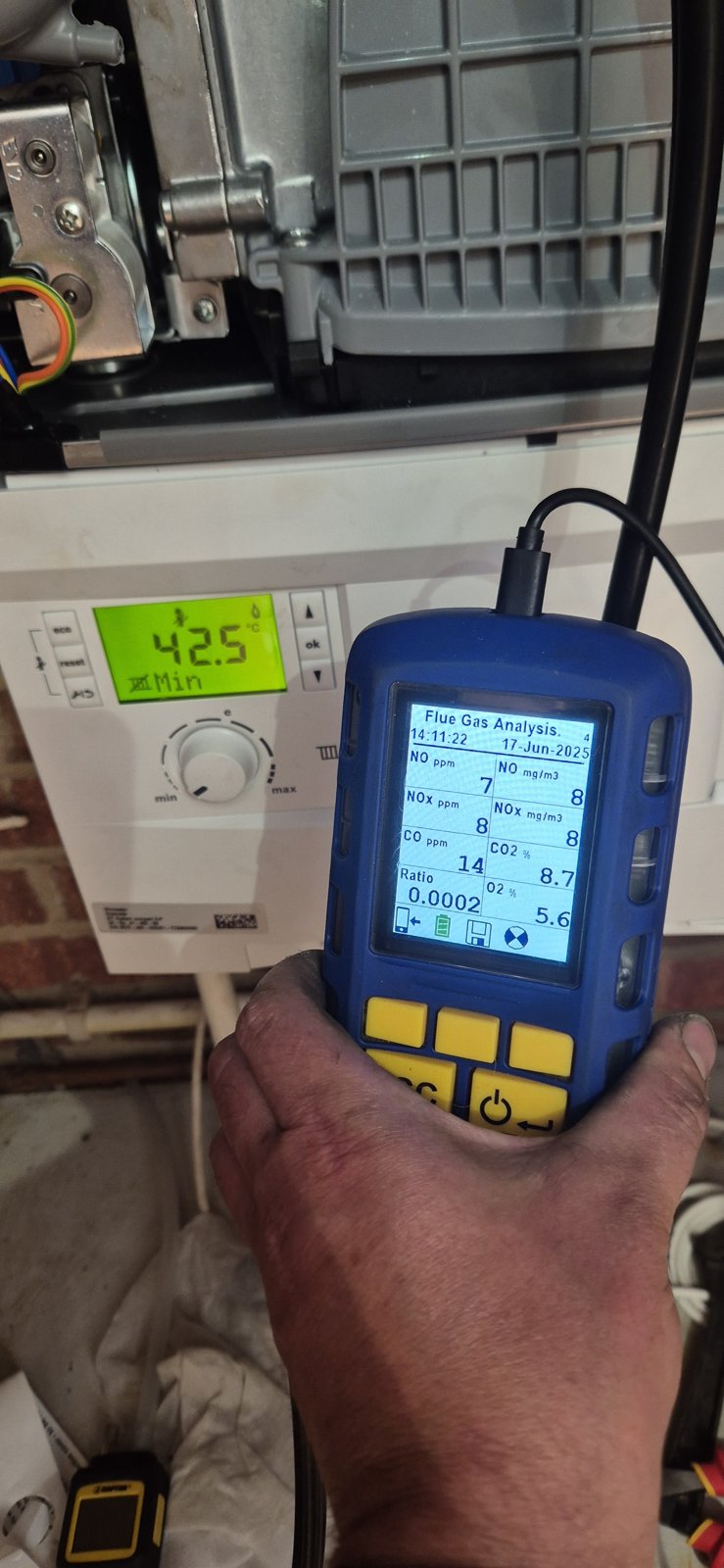 A flue gas analyser held up to a boiler, showing its readings