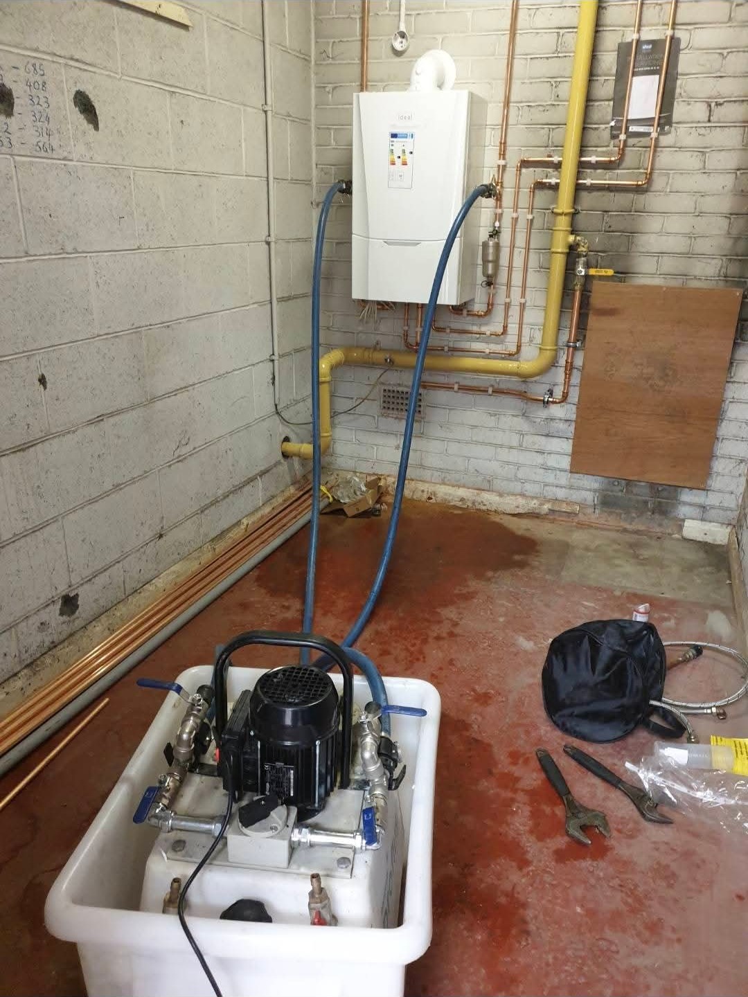 A pump unit connected by hoses to a wall-hung Ideal boiler with copper and gas pipework